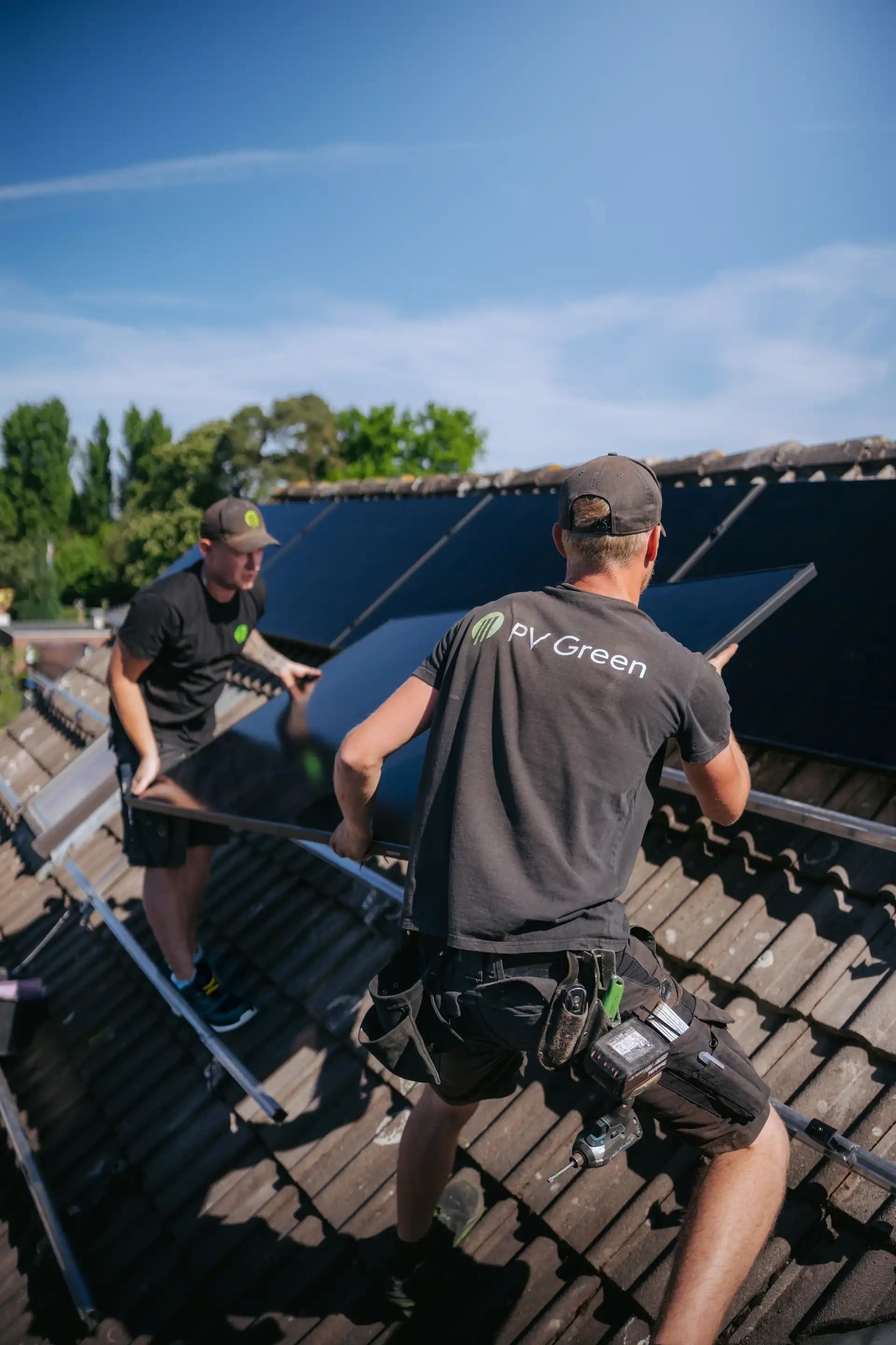 Zwei Monteure reichen ein Solarmodul auf dem Dach an