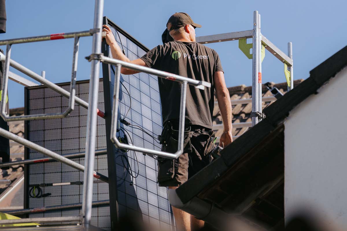 Ein PV Green Dachdecker befindet sich auf einem Dach, hält sich an einem Gerüstfest und blickt zu Kollegen